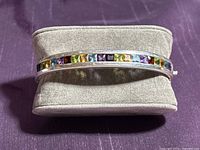 Front view of sterling silver bracelet featuring square-cut multi-colored gemstones set in a channel band, placed on a fabric cushion.