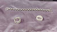 Photo of sterling silver chain link bracelet and 3 rings on purple cloth background.