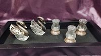 Two sterling silver crystal swans and three sterling silver base salt and pepper shakers shown together on a black display tray.