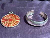 Photo showing the sterling silver hammered cuff bracelet and the Silpada sundial shell pendant side by side on a dark fabric background.