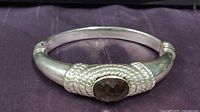 Front view of sterling silver hinged bangle bracelet with faceted oval smoke quartz center stone and textured silver design