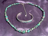 Full view of turquoise and silver beaded necklace with sterling silver cuff bracelet on purple background.