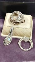 Three wire wrapped jewelry pieces shown in a box: large coiled wire quartz ring, moonstone ring with detailed wire and bead accents, and a round band wire wrap ring.