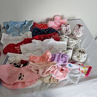 Several Build-A-Bear clothes including skirts, tops, and a fuzzy pink accessory item laid out on a flat surface.