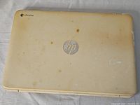 Top view of HP Chromebook laptop showing beige lid with HP and Chrome logos, visible stains and wear marks.