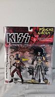 Two KISS Psycho Circus action figures in original sealed packaging. Gene Simmons/The Demon figure with winged outfit and The Ring Master figure with top hat and cane.