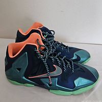 Side and angled view of the pair of Nike LeBron James boys' basketball sneakers showing dark upper, green overlays, coral lining and Nike swoosh detail.