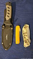 Photo of three cutting utensils: fixed blade knife with nylon sheath, orange handle pocket knife, translucent folding knife.