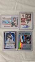 Four autographed sports trading cards in protective sleeves, showing front with signatures and designs.