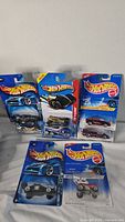 Six Hot Wheels toy cars in blister card packaging on white surface.