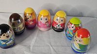 Seven Weebles wobble toy figures arranged in a row on a white surface, varying colors and some with hats or glasses, visible paint details on faces and outfits.
