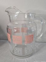 Full view of the clear glass pitcher showing handle, spout and floral panel designs around the pitcher body.