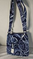 Full front view of the Vera Bradley purse showing blue and white paisley pattern, adjustable strap, front zippered pocket with white zipper pull.