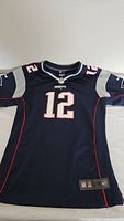 Front view of navy Tom Brady Patriots jersey with number 12 and team logos.