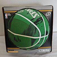 Front view of the green and black Spalding basketball in its box showing the brand and NBA logo, indicating it is new and unopened.