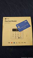 Front view of SumUp Plus Card Reader box showing product image, brand, payment method logos and a blue Visa card sticker.