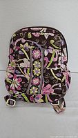 Front view of Vera Bradley backpack showing floral pattern, front zippered pocket, and adjustable straps.