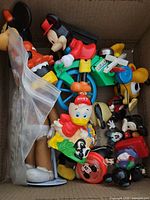 Top-down photo of assorted vintage Disney toys and collectibles in a box showing multiple characters and a green motorcycle toy