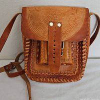 Front view of vintage brown leather Mayan shoulder bag showing hand-tooled detailed calendar design on flap and braided edges with metal rivet strap closure.
