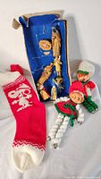 Photo showing boxed vintage wooden nativity pieces next to two knitted elves and a red Snoopy stocking.