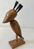 Side angle showing the figural crow bird with black bristle crest and wooden base.