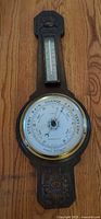 Full view of wall-mounted barometer and thermometer showing entire carved wood case