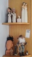 Shelf view showing bobbleheads, Willow Tree style figures, Obama bust, small uniformed man figure and farmer doll