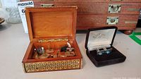 Open inlaid wood box with assorted cufflinks and studs; velvet cufflink case beside