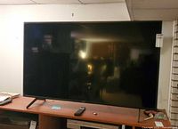 Front view of Sony KD-55X80J TV on stand with remote and accessories visible