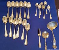 Group shot of all 26 sterling silver flatware pieces on blue background