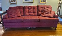 Front view of burgundy three-seat sofa showing cushions, pillows, carved legs