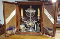 cabinet open showing crucifix, plates, chalice, cruet, spoon, candles, interior lining