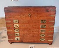 Front view of wooden jewelry chest showing five drawers, brass hardware, ornate scrollwork