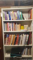 Full bookshelf containing three shelves packed with cookbooks