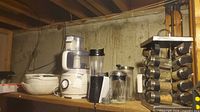 Shelf view showing food processor, blender cup, French press, spice rack, ceramic bowls