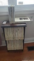 Side table holding two rows of tall white-jacket National Geographic books, additional volumes stacked on top