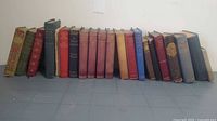 Full row of approximately 20 cloth-bound vintage hardcovers showing varied colors and heights