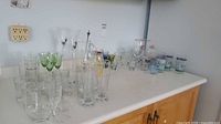 Countertop view of entire glassware assortment with pitcher, spoon, flutes, green stemware, tumblers and highballs