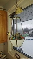 Terrarium hanging by chain in window showing clear and opaque glass panels, artificial birds and feathers inside