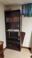 Front view of tall dark brown bookcase showing five shelves and detached back panel