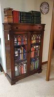 Front view of stained wood bookcase cabinet with glass doors, top drawer visible