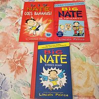 Three Big Nate books by Lincoln Peirce arranged together on a floral patterned cloth background: Big Nate Goes Bananas!, Big Nate Mr. Popularity and Big Nate Strikes Again.