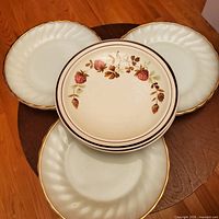 Top view showing three white ridged small plates with gold rim and one floral patterned plate on wooden surface