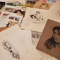 Wide view of multiple sketches and watercolors scattered on table including human figures and rural buildings.