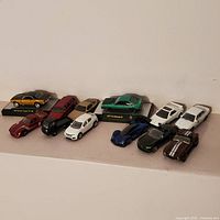 Photo showing 12 assorted Hot Wheels cars arranged in two rows, multi-colored and various styles.