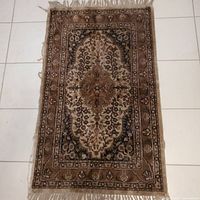 Full front view of the rectangular vintage hand knotted door front rug on tiled floor showing overall pattern and fringe.