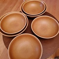 Set of six matte brown ceramic bowls stacked in pairs on a wooden surface, showing overall shape and color.