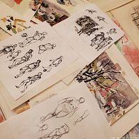 Photo showing multiple sheets of paper with figure sketches mostly in pencil and ink, arranged on a surface.