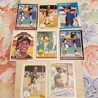 Seven Rickey Henderson MLB baseball cards arranged on floral patterned surface. Cards show Henderson in Oakland A's uniform, various poses including batting and fielding.