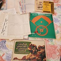 Photo showing the Major League Baseball board game cover, multiple sheets of baseball game stats and scorecards, player rating booklet, rules booklet, and the football book cover.